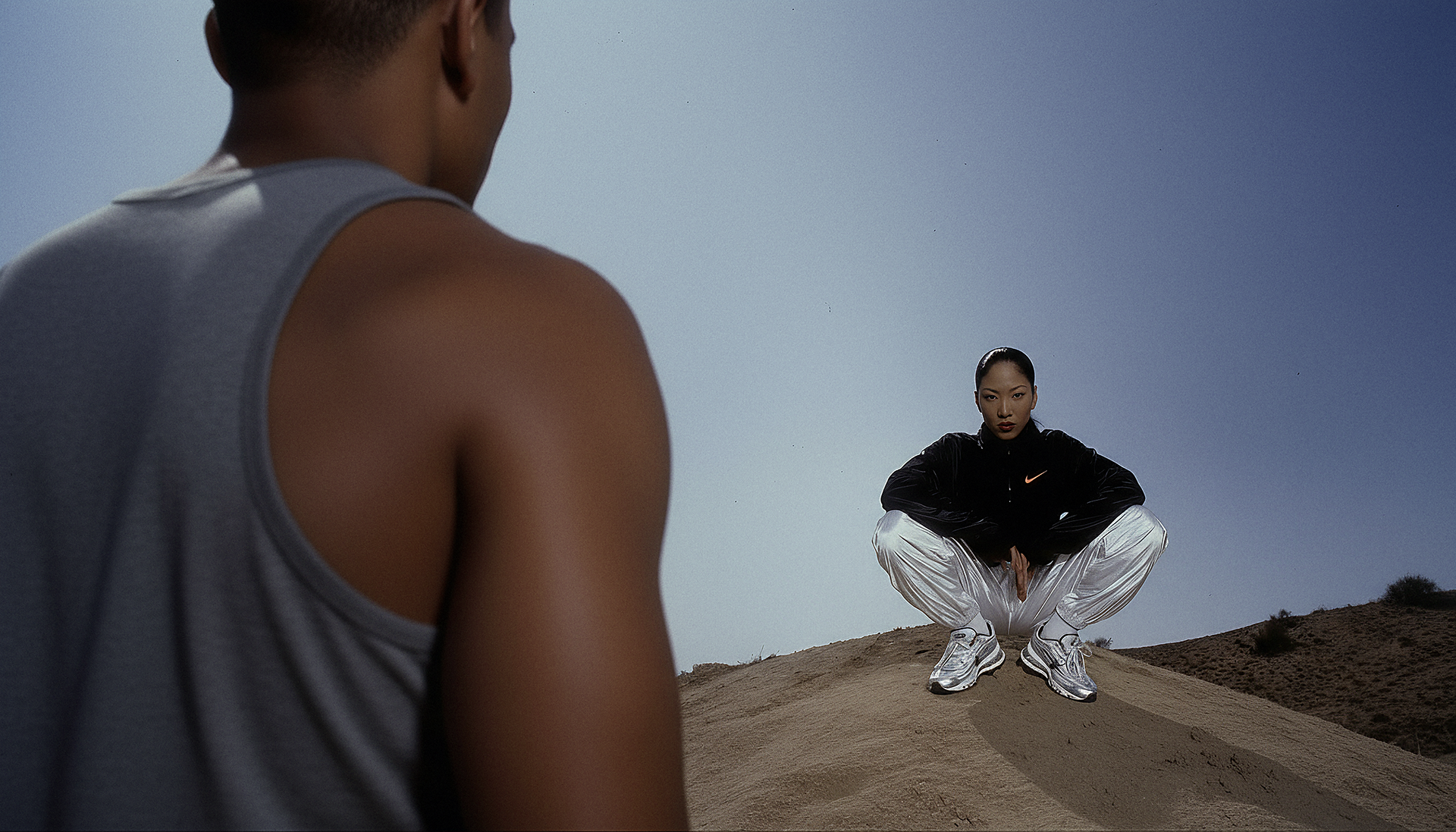 Two athletes facing one another on a sandy hill, with one wearing a Nike jacket